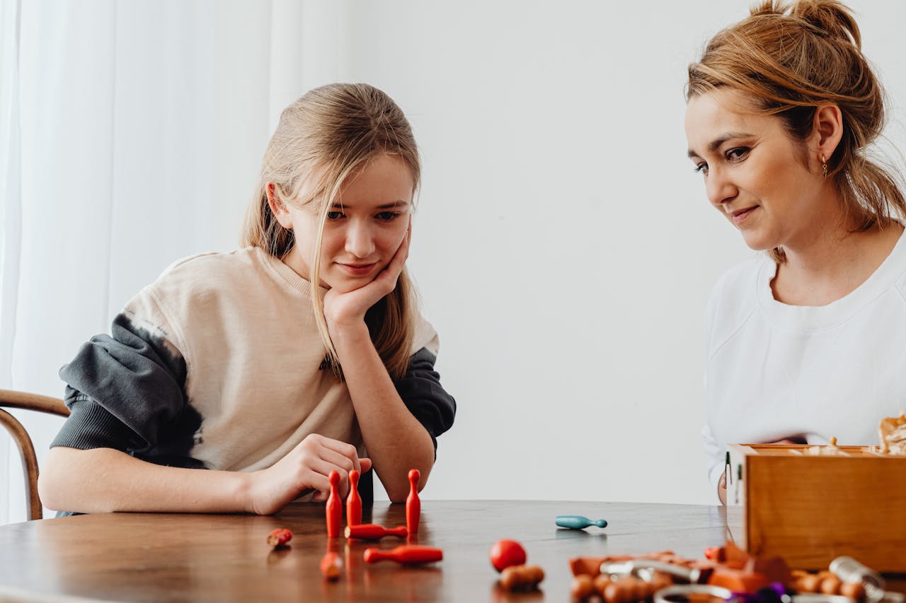 A mother and daughter engage in a playful tabletop game indoors, fostering bonding and creativity.